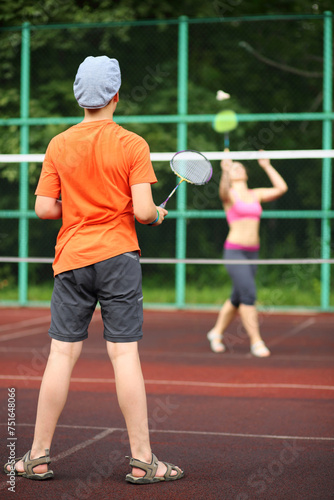 Boy in cap with her mother play badminton on the playground, view from the back. Small depth of focus