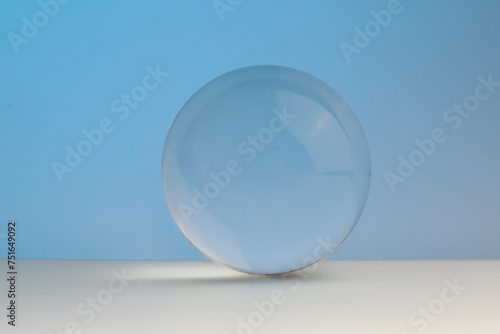 Transparent glass ball on table against light blue background