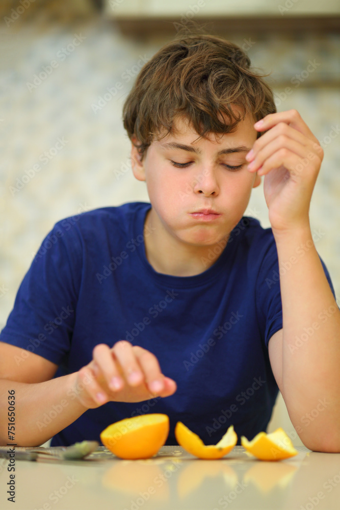 Happy handsome boy teen eats fresh orange in kitchen, shallow dof Happy handsome boy teen eats fresh orange in kitchen, shallow dof