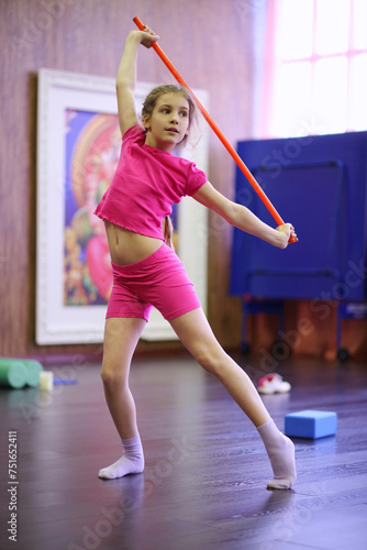 Girl in pink dances with red sport stick in gym hall, shallow dof