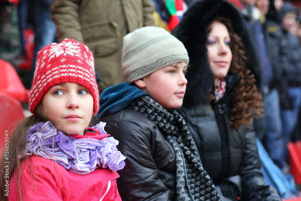 Obraz premium Mother with son and daughter in warm clothing sitting on stadium, focus on girl