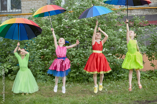 Four girls in dance suits jump throwing up coloured rainbow umbrellas outdoor at lawn photo