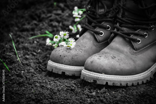 Pair of boots and flowers on soil in the ground in nature