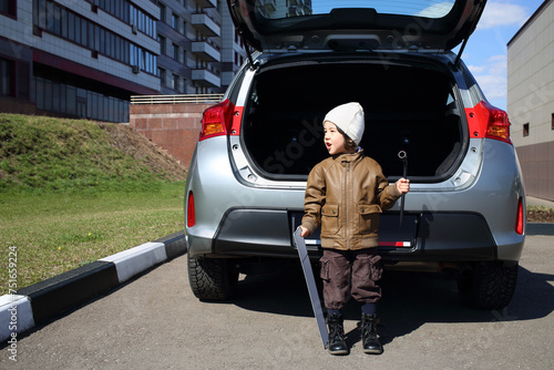 Little boy in white hat standing with machine number and socket wrench near open trunk of car © Pavel Losevsky