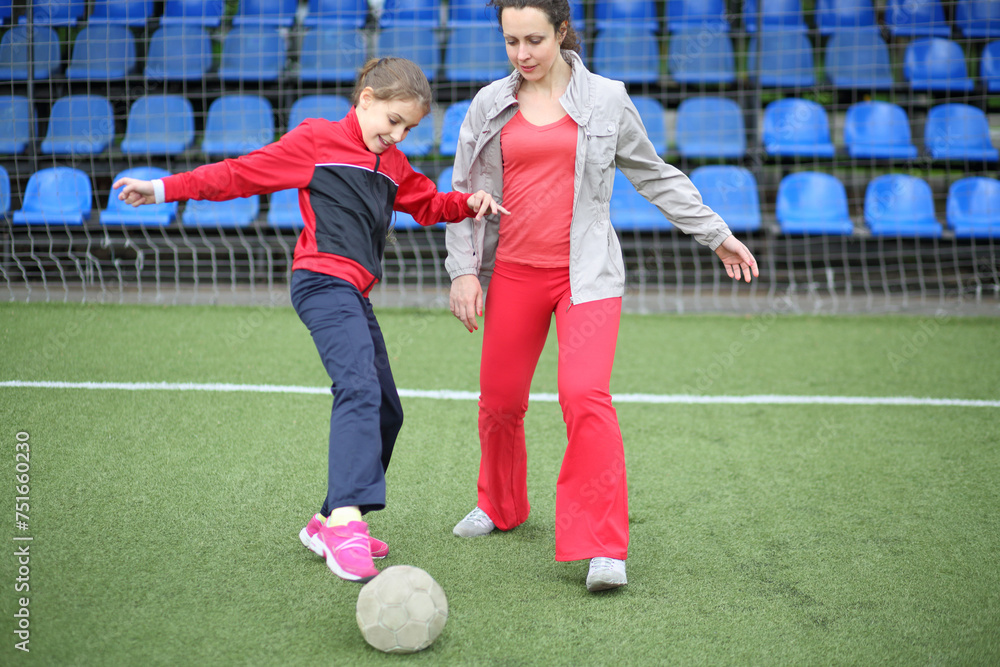 Mother and daughter in tracksuits running with the ball at the stadium