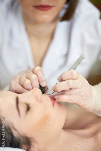 Close-up hands of beautician doing epilation on upper lip of woman lying on couch in beauty salon.