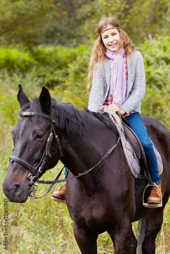 Smiling teenage girl sits on chestnut horse in the park