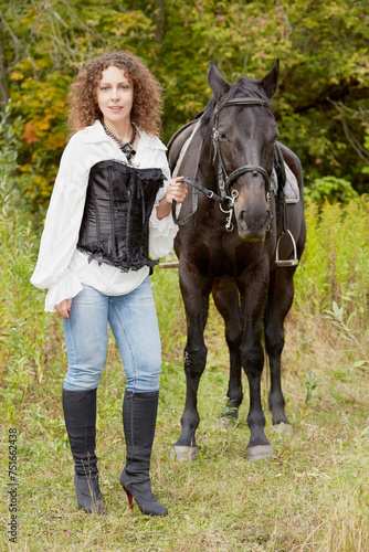 Woman with curly hair stands with bay horse in the park