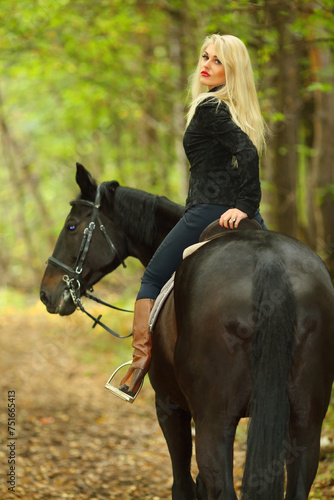 Blonde beautiful woman in black rides horse in green autumn park