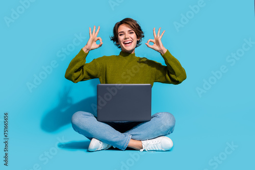 Photo of cheerful glad girl wear stylish clothes sitting floor recommend buy modern device okey sign isolated on cyan color background © deagreez