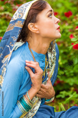 Middle age sad woman in blue sari and Indian adornment poses in garden photo