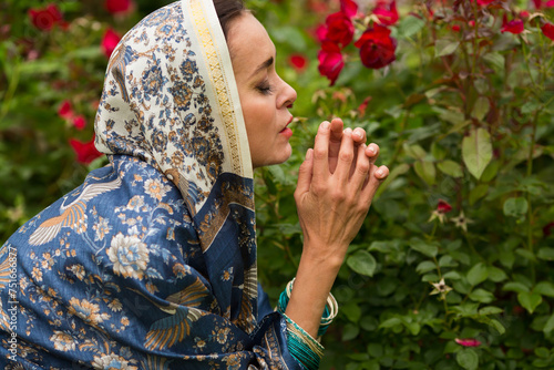 Woman in sari and bracelets prays among red rose bushes in garden photo