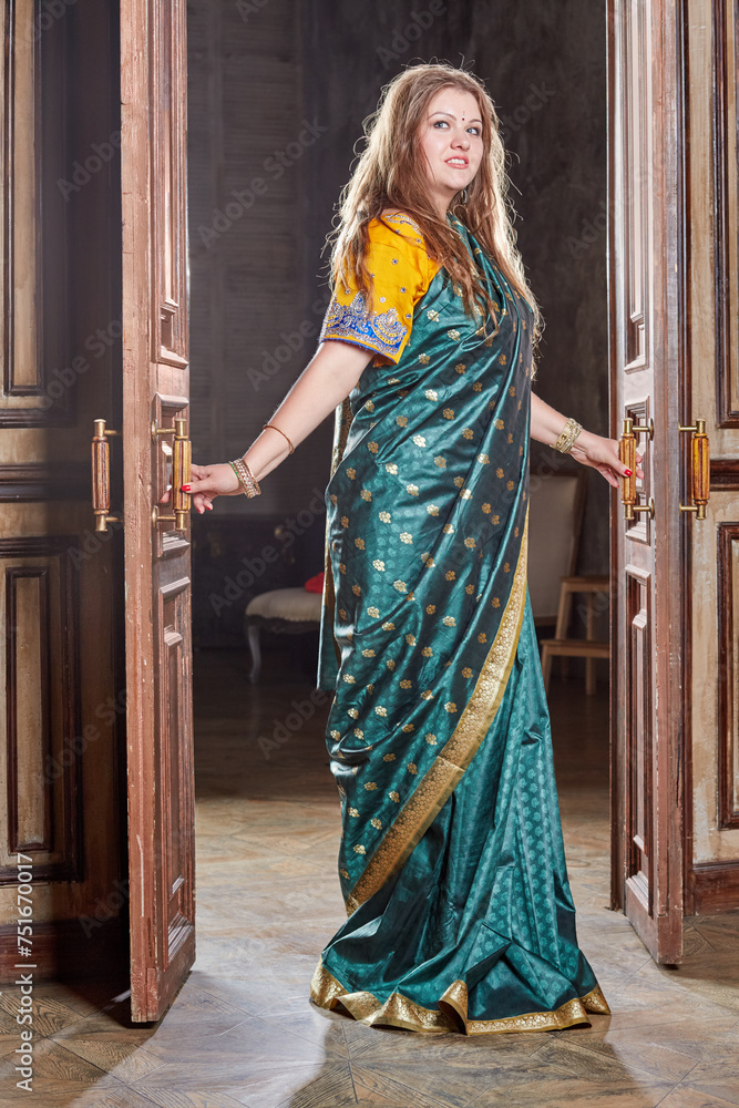 Woman in green with golden dress stands in doorway, holding doors handles