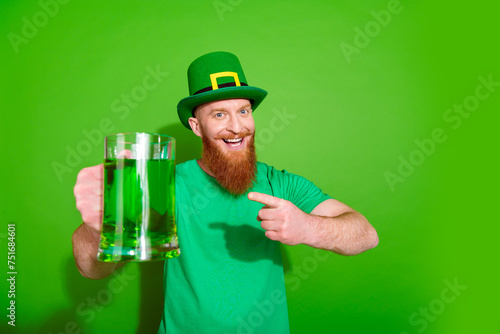 Portrait of funky handsome guy indicate finger beer ginger ale mug empty space isolated on green color background