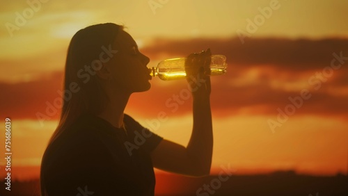Silhouette of a Woman Drinking Water Against a Sunset Background