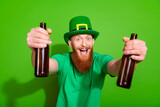 Portrait of cheerful funky young man open mouth hands hold glass beer bottles isolated on green color background