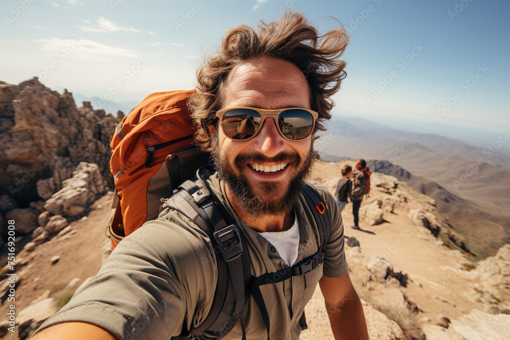 Energetic male hiker with sunglasses taking a selfie on a mountain summit.