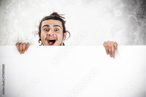 Alternative young man holding a blank banner with amazed expression