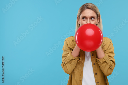 Woman blowing up balloon on light blue background. Space for text