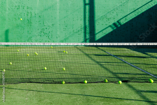 view of a green tennis court with yellow balls and elongated shadows