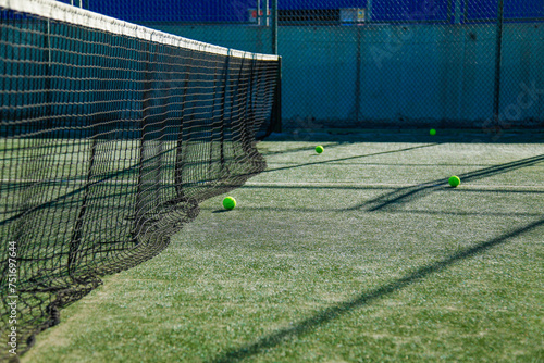 Sunlit tennis court with green balls and net.