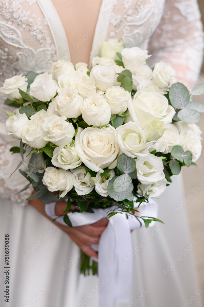 Wedding bouquet of white roses and freesias in the hands of the bride. Bride in a wedding dress holds a bouquet of flowers in front of her. Wedding day concept, happy bride, wedding floristry