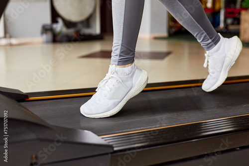 Close-up of a woman's legs in white sneakers on a treadmill. Morning cardio workout. Running in the gym.