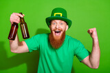 Photo of ecstatic delighted handsome man hold beer bottles raise fist isolated on green color background