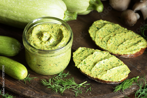 Green zucchini spread in a glass jar with whole wheat bread sandwiches on rustic dark background, healthy summer vegetarian food concept photo