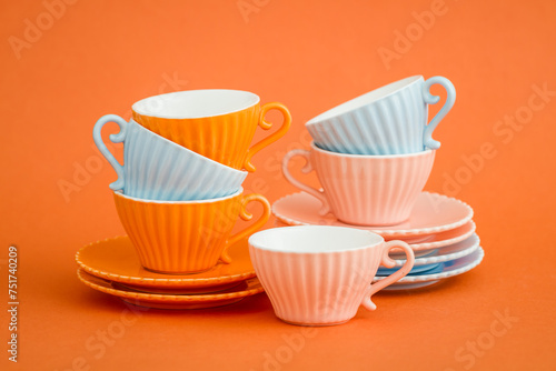 Stacked Light Blue and Pink Coffee Cups with Saucers Against Orange Background.