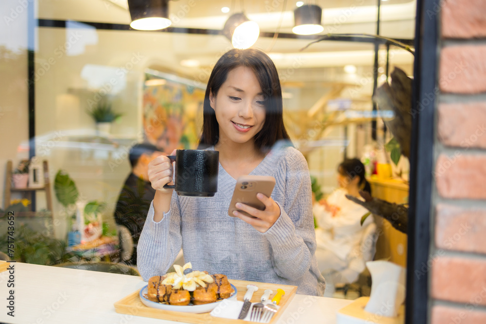 Woman enjoy tea time and use of mobile phone in coffee shop with window reflection