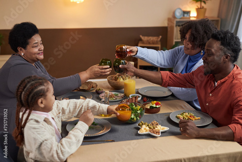 Portrait of three generation African American family enjoying dinner together in cozy home and clinking glasses toasting over table copy space 