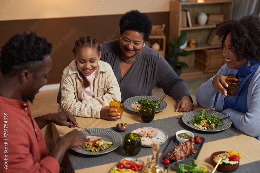High angle view at smiling African American senior woman enjoying dinner with family at table and holding little girl in lap High angle view at smiling African American senior woman enjoying dinner with family at table and holding little girl in lap