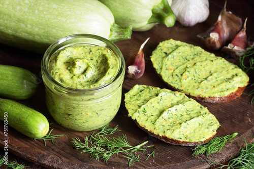 Bild auf Leinwand Green zucchini spread in a glass jar with whole wheat bread sandwiches on rustic