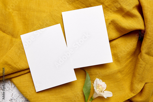 Empty greeting cards and white flower on yellow cloth, top view, flat lay