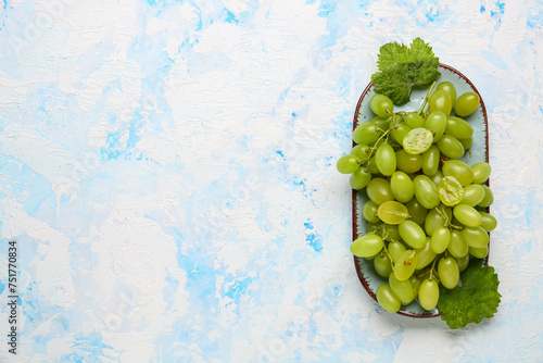 Plate with ripe green grapes and leaves on color background