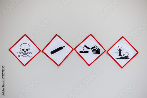 Four hazard warning signs with red diamond borders, depicting toxicity, gas under pressure, corrosion, and environmental hazards, used for safety compliance.