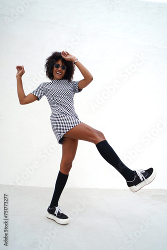 Young woman with afro hairstyle dancing on the white wall. Girl wearing fashionable casual clothes, street style. A lot of copy space.
