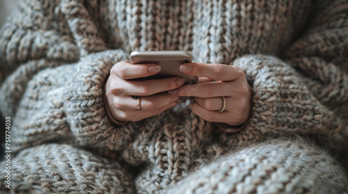 A person in a cozy sweater is focused on their smartphone, interacting with the device in a comfortable indoor setting.