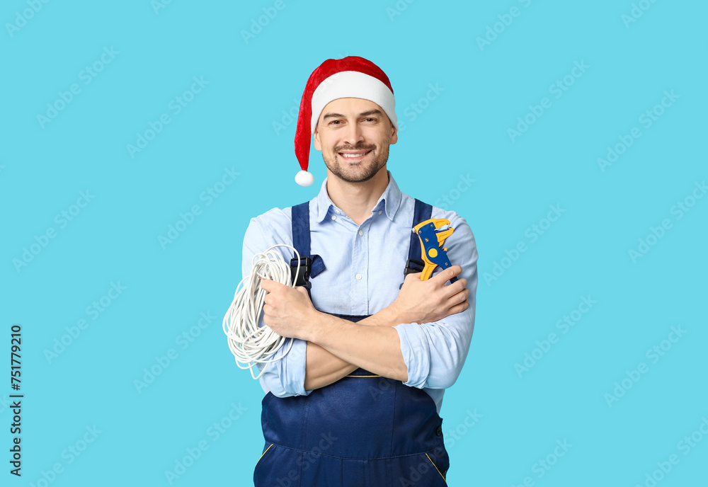 Portrait of male electrician in Santa hat with crimper and wires on blue background