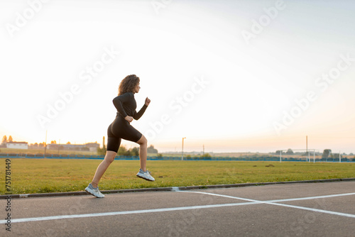 young curly woman athlete jogging at the stadium in summer