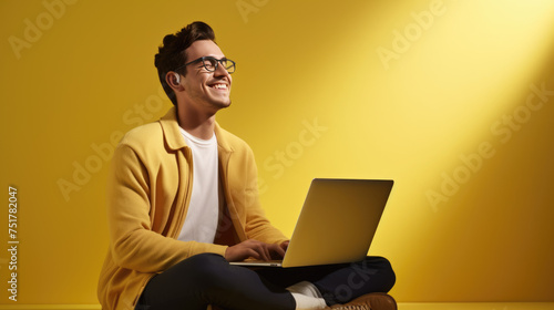 Happy young man working on a laptop against yellow background