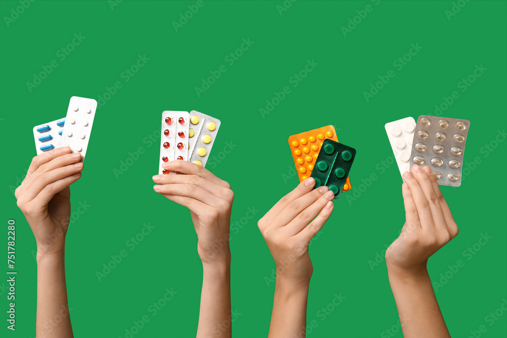 Female hands holding pills in blister packs on green background - obrazy, fototapety, plakaty 