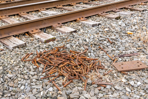Pile of rusty railroad spikes on crushed stone next to railroad tracks.