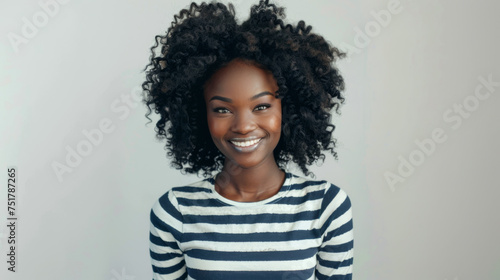 young woman with curly afro hair, wearing a striped shirt, standing with her arms crossed, smiling and looking directly at the camera