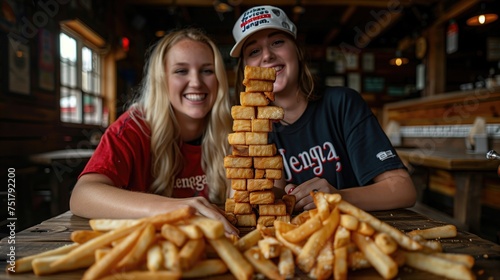 Two friends engage in a game of  fries Jenga   stacking French fries into a precarious tower on the table and taking turns pulling out fries to eat. Fastfood comic situation