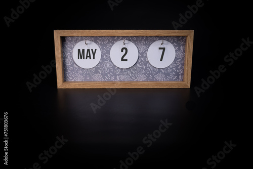 A wooden calendar block showing the date May 27th on a dark black background, save the date or date of an event concept.