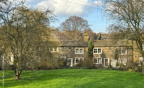 A winter scene of old stone cottages from the early 1800s, surrounded by grass and trees, along Heaton Road in Bradford, Yorkshire, UK.
