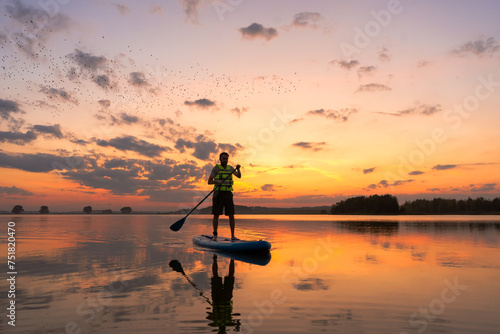 silhouette of man standing on inflatable SUP board and paddling through shining water surface. Wide shot sport man at sunset on a lake photo