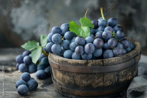 A wooden bucket filled with ripe blue grapes and leaves on a rustic table.